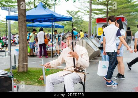 Musicista di strada cinese di mezza età che suona lo strumento musicale cinese tradizionale Erhu (violino cinese) nel Central Park di Shenzhen, Cina Foto Stock