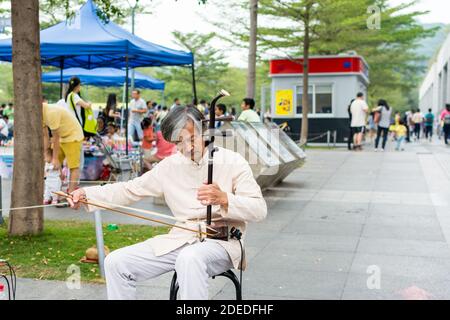 Musicista di strada cinese di mezza età che suona lo strumento musicale cinese tradizionale Erhu (violino cinese) nel Central Park di Shenzhen, Cina Foto Stock