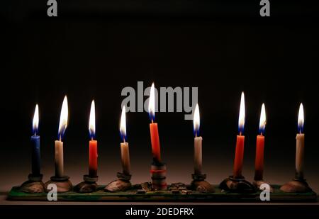 Candele colorate Chanukah illuminate in uno sfondo fatto a casa menorah.black Foto Stock