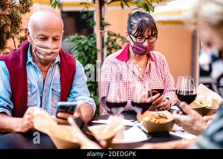 Persone anziane che utilizzano smartphone con maschera coperta - adulti in pensione preoccupati mentre guardano le notizie sullo smartphone - Nuovo stile di vita normale Foto Stock