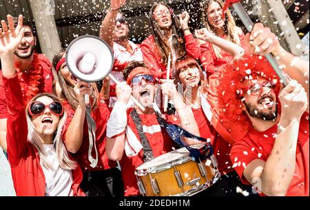 Tifosi di calcio tifosi con bandiera e confetti guardare il calcio Partita - amici gruppi di persone con magliette rosse allo stadio candeggianti Foto Stock