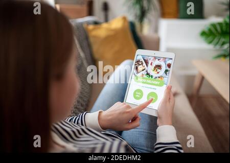 Giovane donna con tablet che ordina cibo a casa, coronavirus e concetto di consegna di cibo. Foto Stock