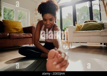 Primo piano ritratto di donna africana che fa esercizio di riscaldamento prima di allenamento a casa Foto Stock