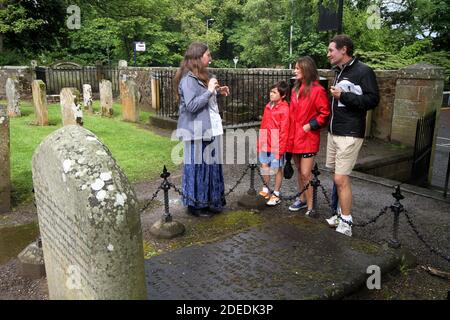 Auld Kirk , Alloway, Ayrshire, Scozia, Regno Unito. 24 maggio 2014. Un narratore nel cimitero che parla con una giovane famiglia, madre, padre, figlio imparando la storia delle tombe associate con il poeta Robert Burns Foto Stock