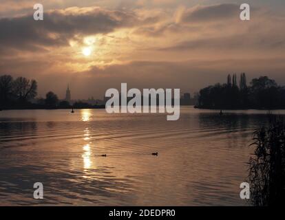 Potsdam, Germania. 27 Nov 2020. Il sole che tramonta può essere visto in una lacuna tra le nuvole e riflette la sua luce nell'acqua del lago profondo attraverso il quale scorre l'Havel. Sullo sfondo, è visibile la sagoma del centro della città con la chiesa di San Nikolai e la Heiliggeistkirche (l). Credit: Soeren Stache/dpa-Zentralbild/ZB/dpa/Alamy Live News Foto Stock