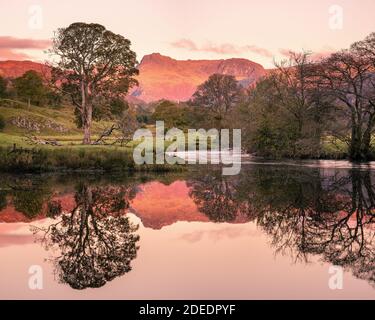 Paesaggio del Distretto dei Laghi con il lago Elterwater e i Langdale Pikes Illuminato dal bagliore rosso dell'alba a Langdale Cumbria Foto Stock