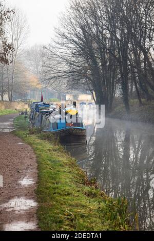 Barche di canale ormeggiate accanto all'alzaia del canale Kennett e Avon in una giornata invernale foggosa. Bradford on Avon, Wiltshire, Inghilterra, Regno Unito Foto Stock