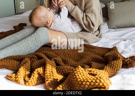 Carina bambina caucasica sdraiata su un letto accogliente con la madre vestita di maglia colore marrone maglione. Rimani a casa durante la quarantena di Coronavirus covid-19 Foto Stock