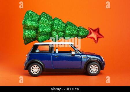 Albero di Natale di Capodanno con stella rossa sulla parte superiore del tetto blu del giocattolo dell'auto. Sfondo arancione. Albero di Natale creativo in miniatura su auto Foto Stock