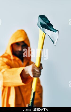 AX nelle mani dell'uomo. Concentrarsi sulla lama. Il maschio in arcobaleno arancione minaccia con l'ascia. Concetto di emozioni Foto Stock