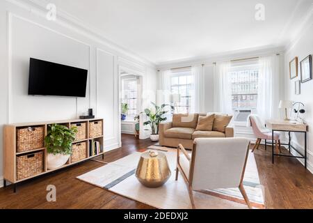 Un luminoso, bianco soggiorno in un condominio del centro con arredamento accogliente, un televisore montato sulla parete, e un tappeto seduto su pavimenti in legno. Foto Stock