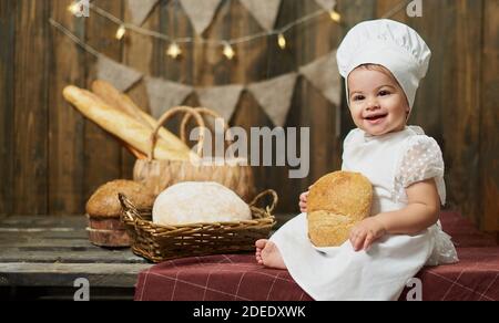 Adorabile panettiera per bambina con pane fresco sullo sfondo di un muro di legno e pane Foto Stock