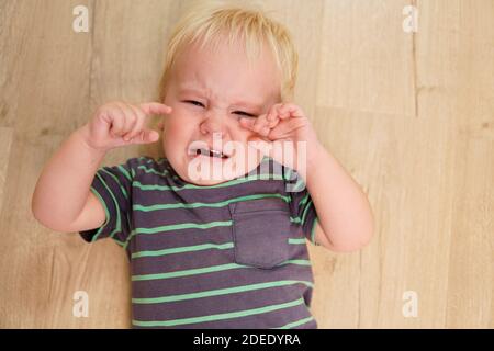 Ragazzino con capelli biondi piange sul pavimento. Alta qualità Foto Stock