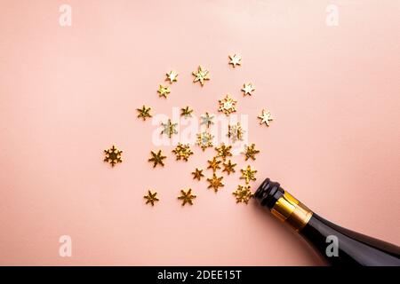 Bottiglia di champagne con spruzzi dorati scintillanti su sfondo rosa. Disposizione piatta, vista dall'alto, stile natalizio alla moda. Foto Stock