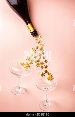 Bottiglia di champagne con spruzzi dorati scintillanti e bicchieri di champagne su sfondo rosa. Disposizione piatta, vista dall'alto, stile natalizio alla moda. Foto Stock