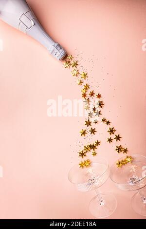 Bottiglia di champagne con spruzzi dorati scintillanti e bicchieri di champagne su sfondo rosa. Disposizione piatta, vista dall'alto, stile natalizio alla moda. Foto Stock