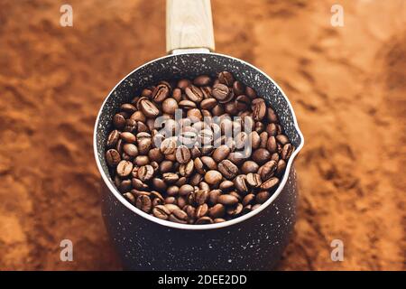 Sullo sfondo del caffè macinato si trova una spotty cezve riempita con chicchi di caffè aromatici tostati, che poi saranno fatti in un espresso forte. Foto Stock