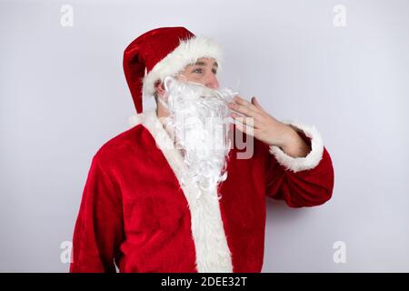 Uomo vestito come Babbo Natale in piedi su isolato sfondo bianco sorpreso coprendo la bocca con la mano Foto Stock