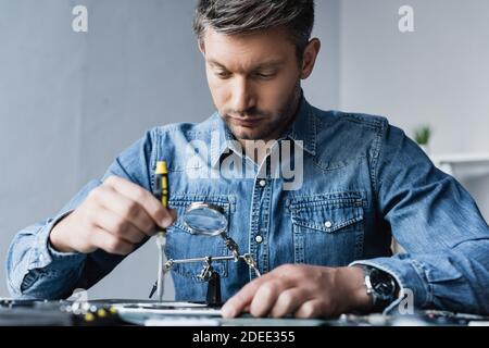 Addetto alla riparazione con cacciavite che fissa il telefono cellulare sul luogo di lavoro primo piano sfocato Foto Stock