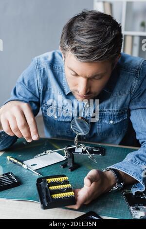 Riparatore che guarda il supporto con punte per cacciavite sul posto di lavoro con telefoni cellulari smontati su sfondo sfocato Foto Stock