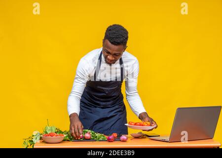 chef africano che prepara un pasto e utilizza il suo computer portatile Foto Stock