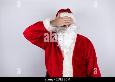 Uomo vestito come Babbo Natale in piedi su isolato sfondo bianco serietà e coprendo gli occhi con la mano Foto Stock