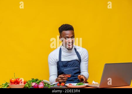 eccitato chef africano guardando il suo laptop mentre tiene un carta di credito Foto Stock