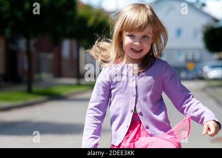 Bambino felice che corre verso la fotocamera che salta. Sorridente allegra ragazza attiva con i capelli volanti dissipati che si muovono velocemente verso la fotocamera, primo piano Foto Stock