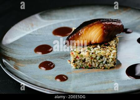 pesce alla griglia con riso e verdure su sfondo nero Foto Stock