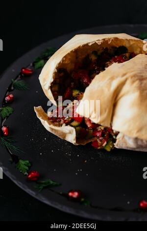 Insalata di verdure georgiane in pane di tortilla su sfondo nero Foto Stock