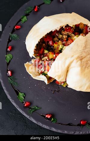 Insalata di verdure georgiane in pane di tortilla su sfondo nero Foto Stock