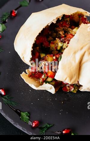 Insalata di verdure georgiane in pane di tortilla su sfondo nero Foto Stock