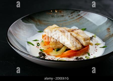 filetto di merluzzo alla griglia con verdure e salsa su un nero sfondo Foto Stock