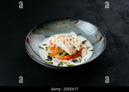 filetto di merluzzo alla griglia con verdure e salsa su un nero sfondo Foto Stock
