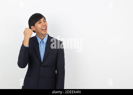 Eccitato giovane bell'uomo d'affari asiatico alzando i suoi pugni con sorridente, celebrando il successo isolato su sfondo bianco. Foto Stock