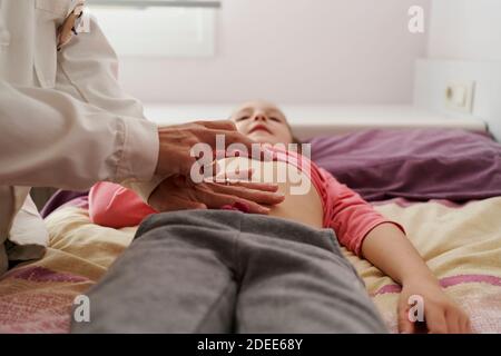 Dottore femmina che esamina l'addome di una bambina nella sua stanza. Concetto medico domestico Foto Stock