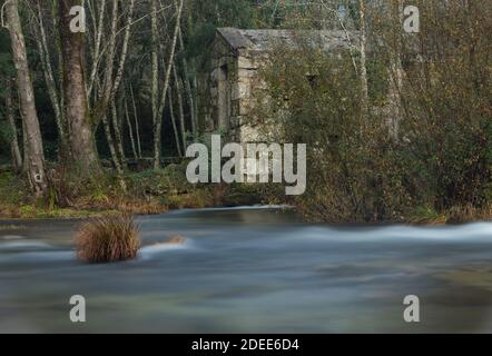 Mulino ad acqua in pietra abbandonato sul letto del fiume Cavado. Scatto a lunga esposizione. Foto Stock