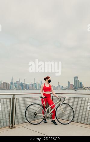 Giovane ciclista femminile che indossa maschera facciale con bicicletta sul lungomare Foto Stock