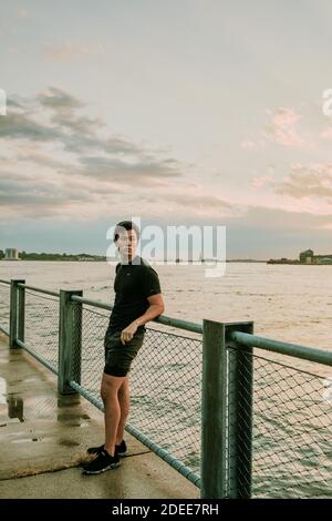 Atleta maschile rilassante sul lungomare durante il tramonto. Foto Stock