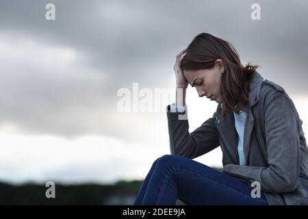 Profilo di una donna triste che lamenta la seduta da sola in un giorno nuvoloso Foto Stock