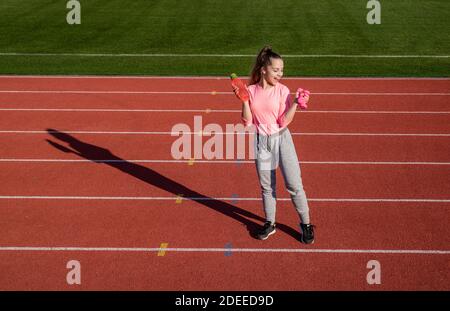 teen ragazza allenamento con manubri e bottiglia d'acqua allo stadio all'aperto, fitness. Foto Stock