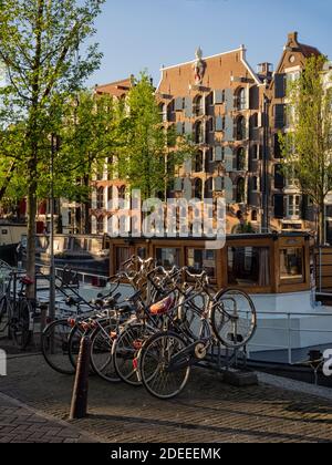 AMSTERDAM, PAESI BASSI - 01 MAGGIO 2018: Biciclette parcheggiate su Brouwersgracht con vista delle barche e dei magazzini lungo il canale sullo sfondo Foto Stock