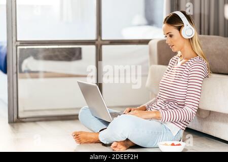Giovane donna con cuffie e computer portatile sul divano Foto Stock