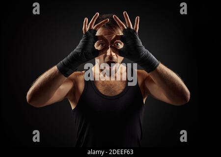 Bell'uomo bearded fit che mostra un gesto divertente su sfondo nero Foto Stock