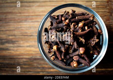 Chiodi di garofano secchi in una ciotola su sfondo di legno. Chiodo di garofano per favorire. Foto Stock