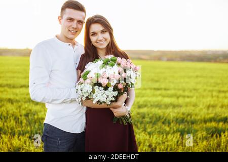 giovane coppia felice in amore, ragazza che tiene fiori, felice e godere l'una dell'altra azienda, pubblicità, Foto Stock