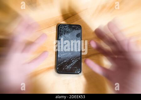 Concetto di caduta smart phone con schermo rotto. Vista dall'alto sulla scrivania in legno sfondo. Incrinato, in frantumi lcd touch screen sul moderno cellulare. Gadget Foto Stock