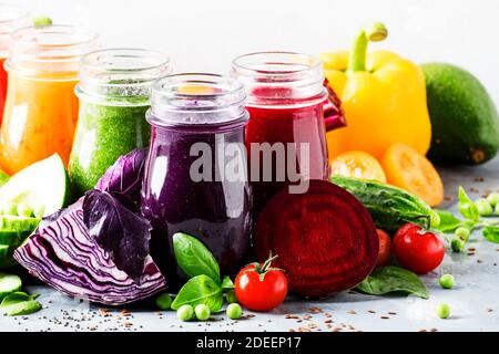 Succhi e frullati di verdure vegan multicolore in bottiglie di vetro su tavola grigia, fuoco selettivo Foto Stock