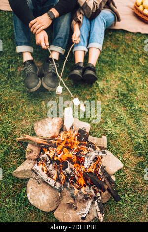 Gambe di coppia vicino al fuoco che stanno arrostendo marshmallows. Concetto di picnic Foto Stock