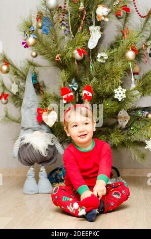 felice ragazzino seduto sotto l'albero di natale Foto Stock